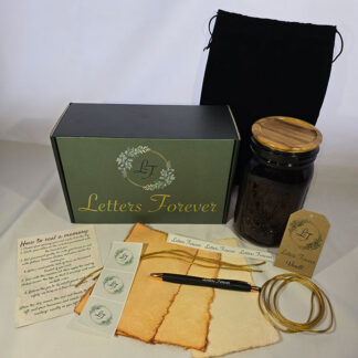 The Memory Vault gift set includes a green box, black drawstring bag, glass jar with wooden lid, parchment paper, pen, stickers, tags, gold string, and an instruction sheet—all neatly arranged.